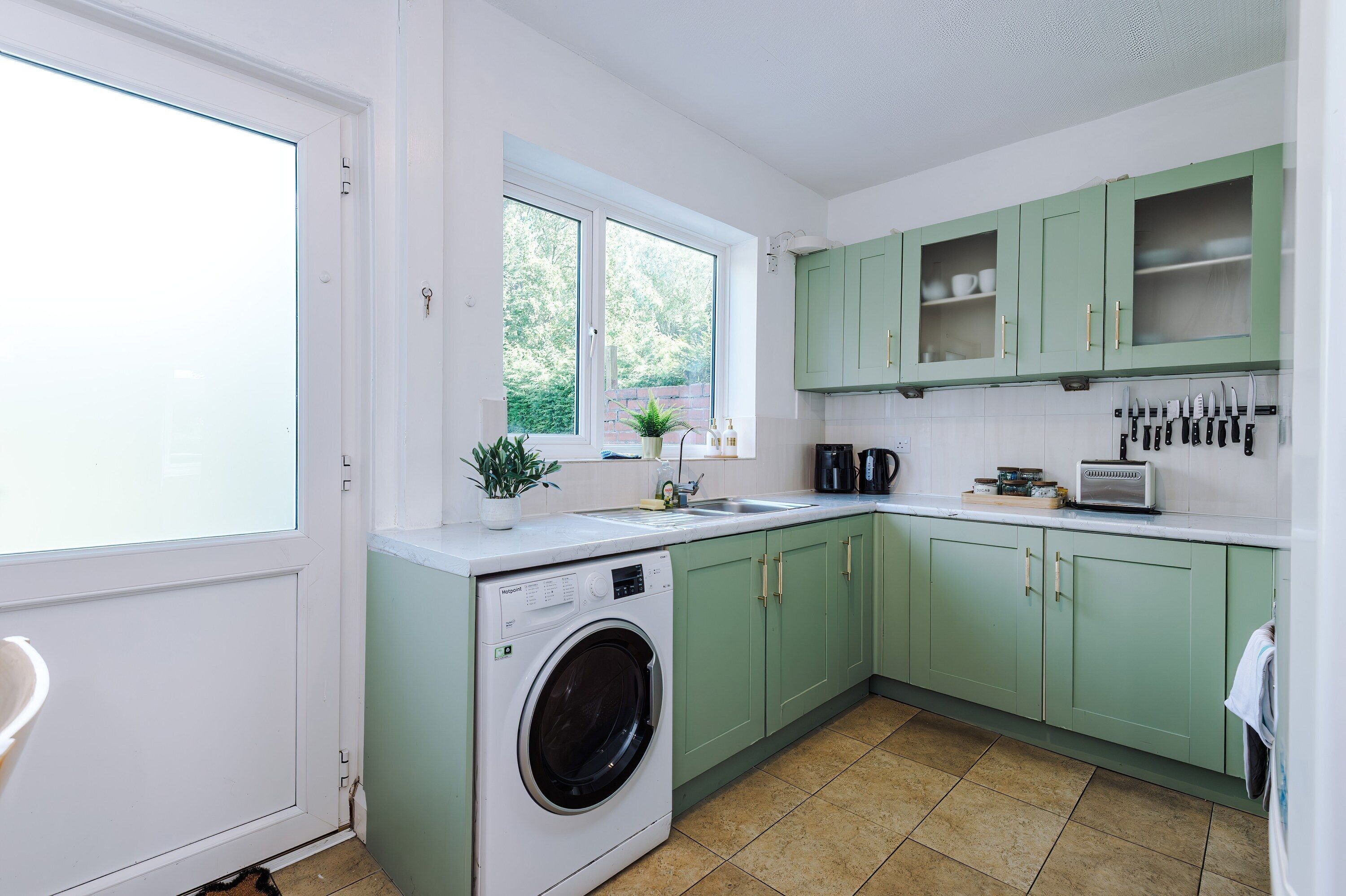 A compact kitchen with a washing machine, a sink, and green cabinets.