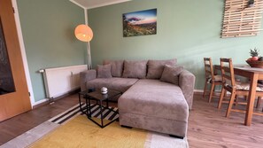 A modern living room with a sectional sofa, a small table, and a dining area with wooden chairs.