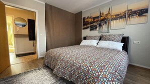 Ett sovrum med en stor säng, en väggpanel av träribbor och tre tavlor som föreställer stadsvyer.