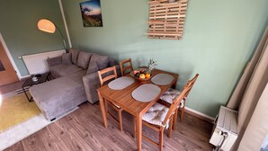 Ett mysigt vardagsrum med en soffa, ett matbord med stolar, en fruktskål och ett träställ på väggen.