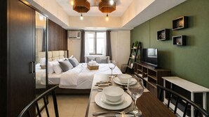Camera d'albergo moderna con un letto, comodino, televisore e zona pranzo apparecchiata con piatti, bicchieri e posate.