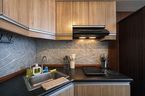 A modern kitchen with wooden cabinets, a stainless steel sink, and a black countertop. - Evergreen Haven Studio | Prime IT Park Spot (Cebu City)