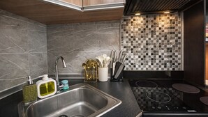 A modern kitchen with a stainless steel sink, a black induction cooktop, and a backsplash with a mosaic tile pattern. - Noirwood Studio | IT Park Pool + Fast WiFi (Cebu City)