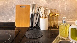 Een keukentafel met een snijplank, messen, lepels en een fles afwasmiddel.