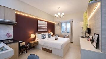 A modern hotel room with a bed, bedside tables, a desk, a chair, a chandelier, and a window with curtains.