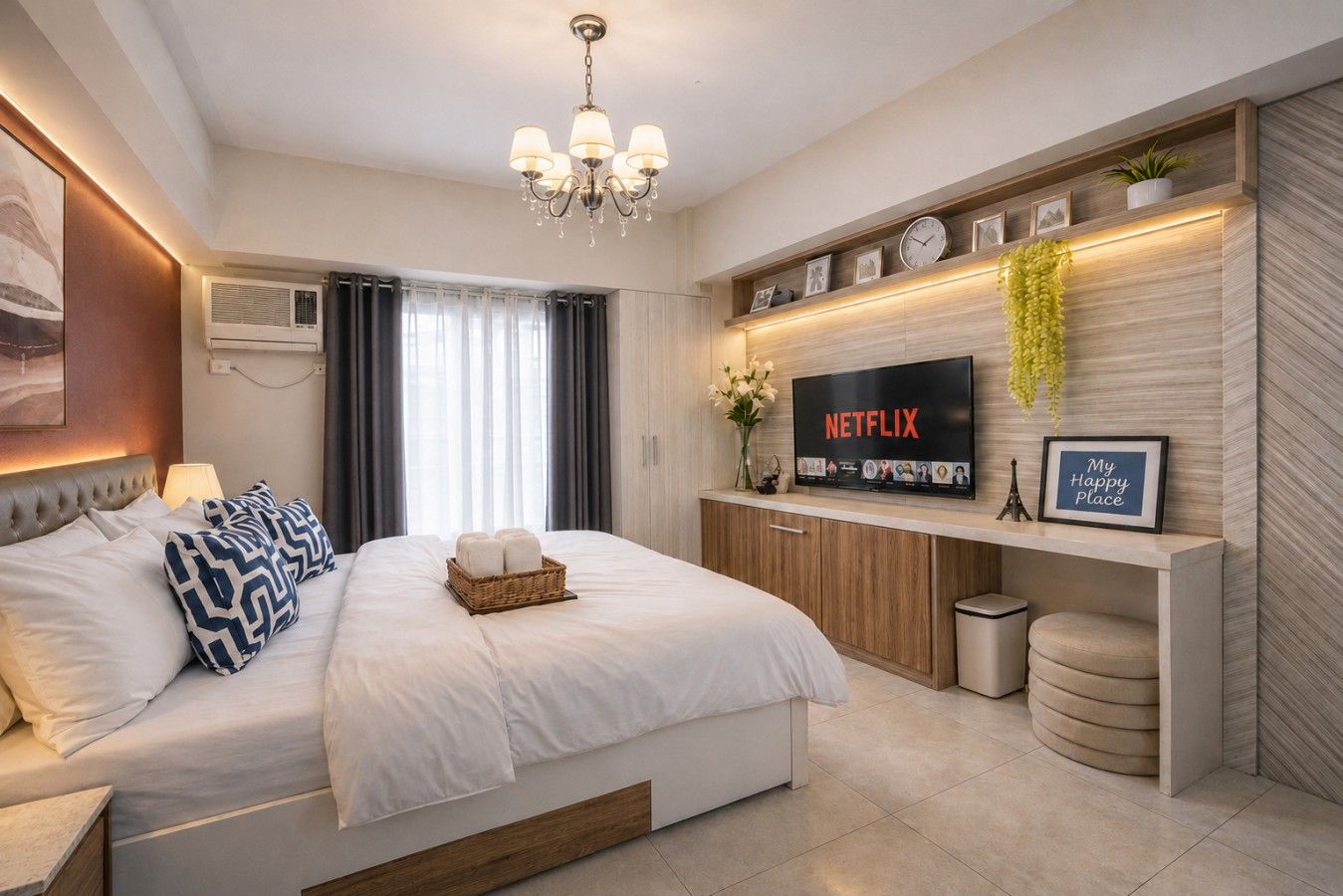A modern hotel room with a large bed, a flat-screen TV, a wall-mounted shelf with decorative items, and a bedside table with a lamp.