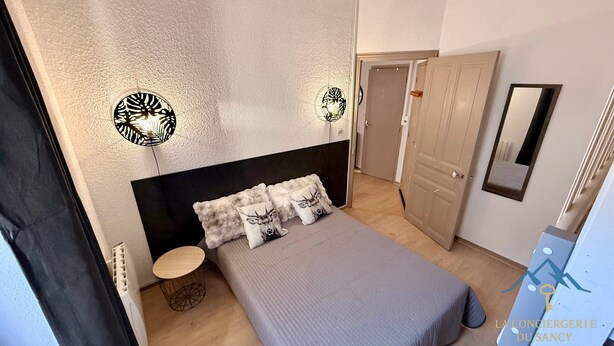 Un dormitorio con una cama, una mesa redonda de madera y dos apliques.