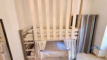 Una litera con estructura de madera, ropa de cama blanca y una cortina.