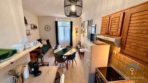Cocina compacta con zona de comedor, muebles de madera y una lámpara moderna.