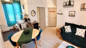 Un espacio habitable compacto con comedor, kitchenette, sofá y una mesita de centro.