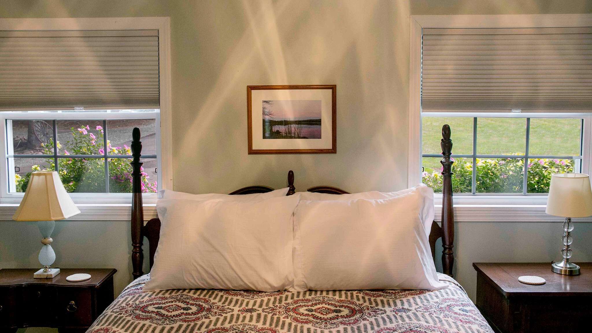Une chambre à coucher avec un lit, deux tables de chevet, une fenêtre avec des stores et un tableau encadré au mur.