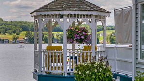A gazebo with yellow chairs and a hanging flower basket, overlooking a lake with boats and houses in the background. - Sun Fun and Waneta (Dundee)