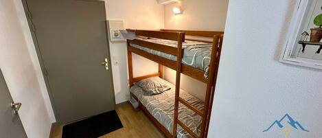 Ein Zimmer mit einem Etagenbett, einer Tür, einer Wandleuchte und einem kleinen Fenster mit einer Pflanze.