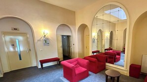 Un hall de hotel con sofás rojos, un banco, un espejo grande y puertas en arco.