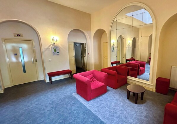 A hotel lobby with red sofas, a bench, a large mirror, and arched doorways. - La Rive Gambetta La Bourboule 4 Pers (La Bourboule)