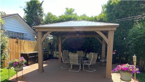 Eine überdachte Terrasse mit Tisch und Stühlen, umgeben von einer Holzterrasse und einem Rasen.