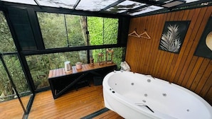 Eine Holzterrasse mit einer großen weißen Badewanne, Holzbanken und einer hängenden Leuchte.
