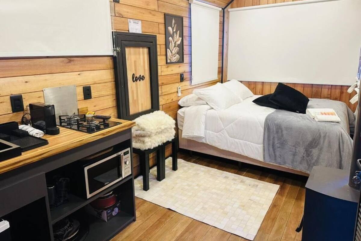 Ein kleines Zimmer mit einem Bett, einem kleinen Schreibtisch mit Wasserkocher, Mikrowelle und einer Holzwand mit einem gerahmten Bild.