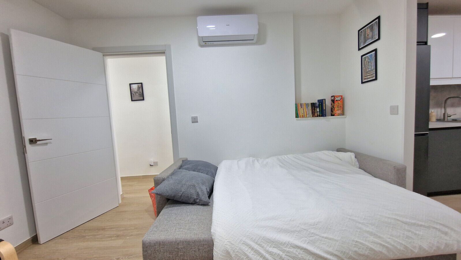 A bedroom with a bed, a grey sofa, a white wardrobe, and a small kitchenette.