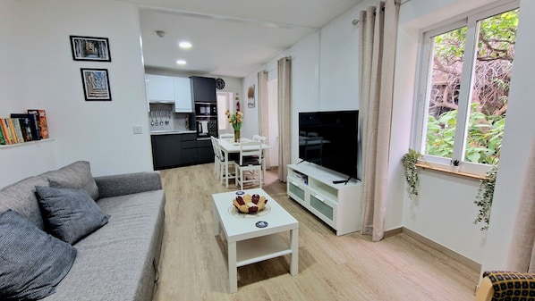 Un salon moderne avec un canapé gris, une table basse, un téléviseur et une cuisine en arrière-plan.