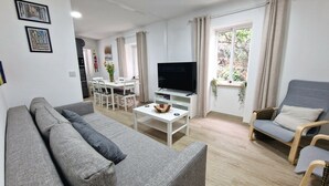 A modern living room with a grey sofa, a TV on a white stand, a dining area with white chairs, and a window with curtains. - old town experience like no other (Gibraltar)