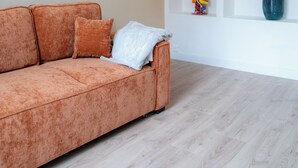 Un salón con un sofá, una lámpara colgante y un estante blanco con objetos decorativos.