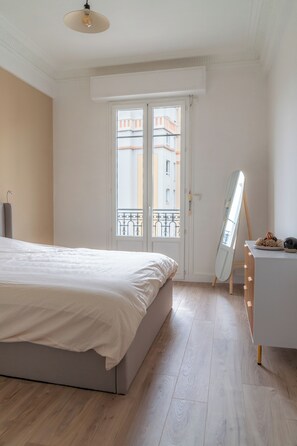 A bedroom with a bed, a dresser, a mirror, and a window with a view of buildings. - New & Elegant Apartment - Haut Musiciens   (Nice)