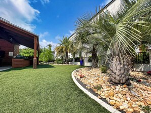 A patio area with artificial grass, a stone pathway, and a palm tree.