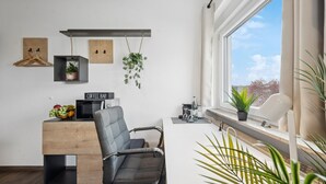 Une chambre moderne équipée d’un bureau, d’une chaise, de plantes en pot et d’une fenêtre donnant sur un beau paysage.