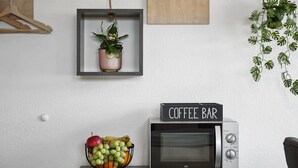 Un four à micro-ondes avec une pancarte indiquant « Coin café », un panier de fruits, une plante suspendue et un cintre en bois accroché au mur.