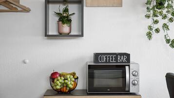 Eine Mikrowelle mit einem 'Coffee Bar' Schild, eine Obstschale, eine hängende Pflanze und ein Holzaufhänger an der Wand.