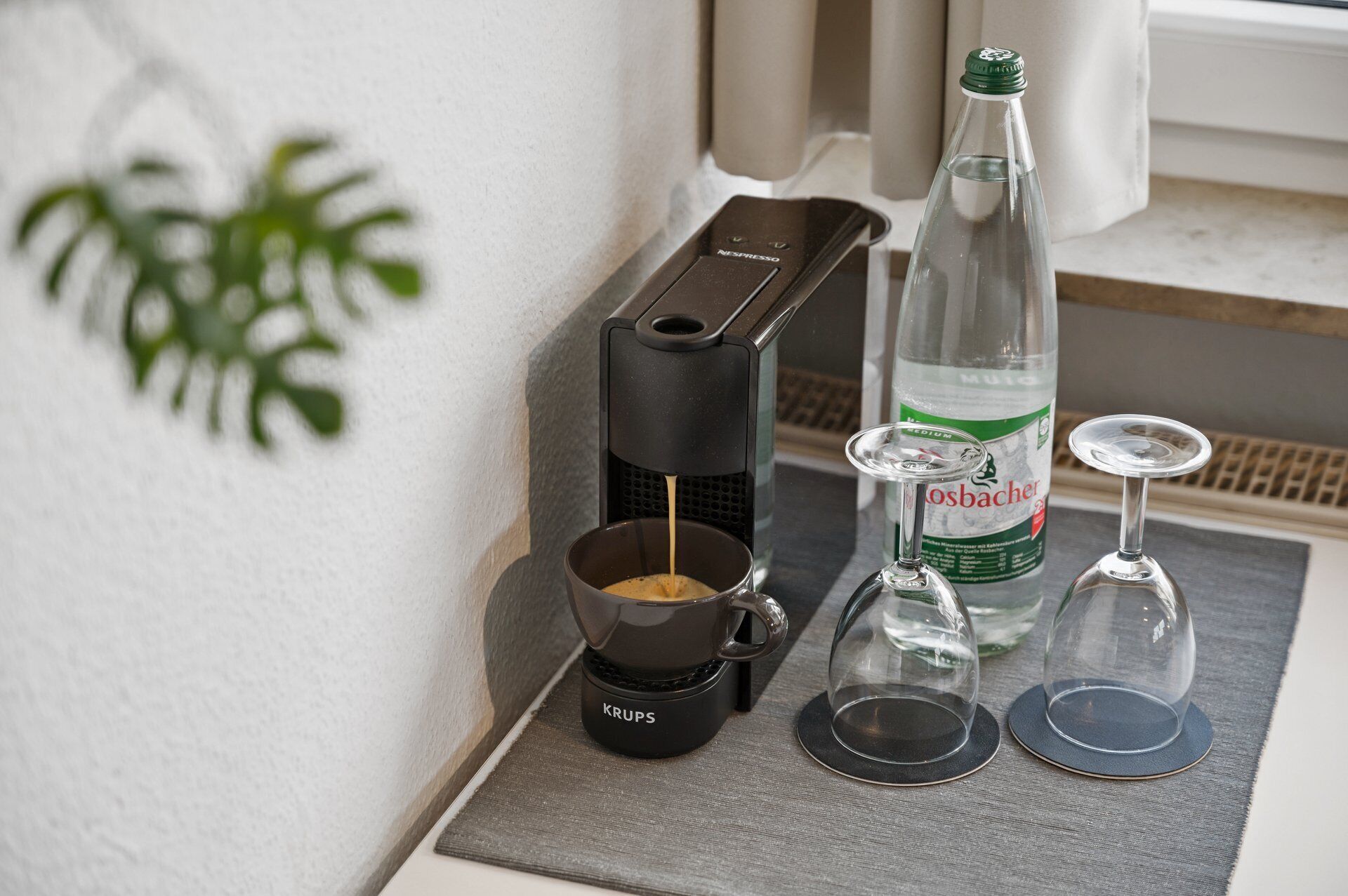 Une machine à café, une bouteille d’eau et deux verres à vin sont posés sur une table.
