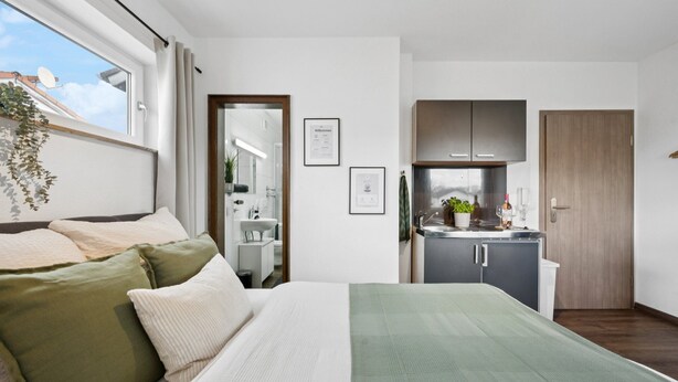 Une chambre avec un lit, une fenêtre avec des rideaux, une vue sur le ciel, une salle de bain et un coin cuisine.