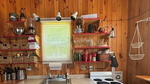 Een kleine keuken met een kookplaat, spoelbak en planken vol keukenbenodigdheden.