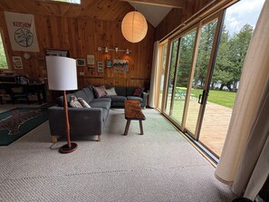 A cozy living room with a sofa, a lamp, and a view of the outdoors. - Loon-R Landing on paddle only Daniels Pond in Glover, Vermont (Glover)