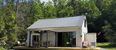 A modern house with a covered patio, large windows, and a view of the surrounding forest.