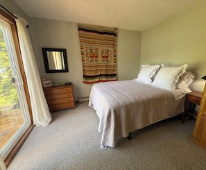 A bedroom with a bed, a dresser, a mirror, and a window with curtains.