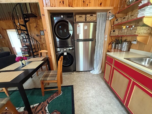 A compact kitchen with a washing machine, a refrigerator, and a dining area with a table and chairs. - Loon-R Landing on paddle only Daniels Pond in Glover, Vermont (Glover)