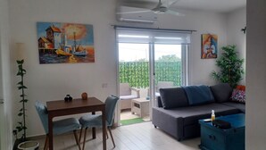 Een woonkamer met een bank, een eettafel met stoelen, een plafondventilator en een schilderij aan de muur.
