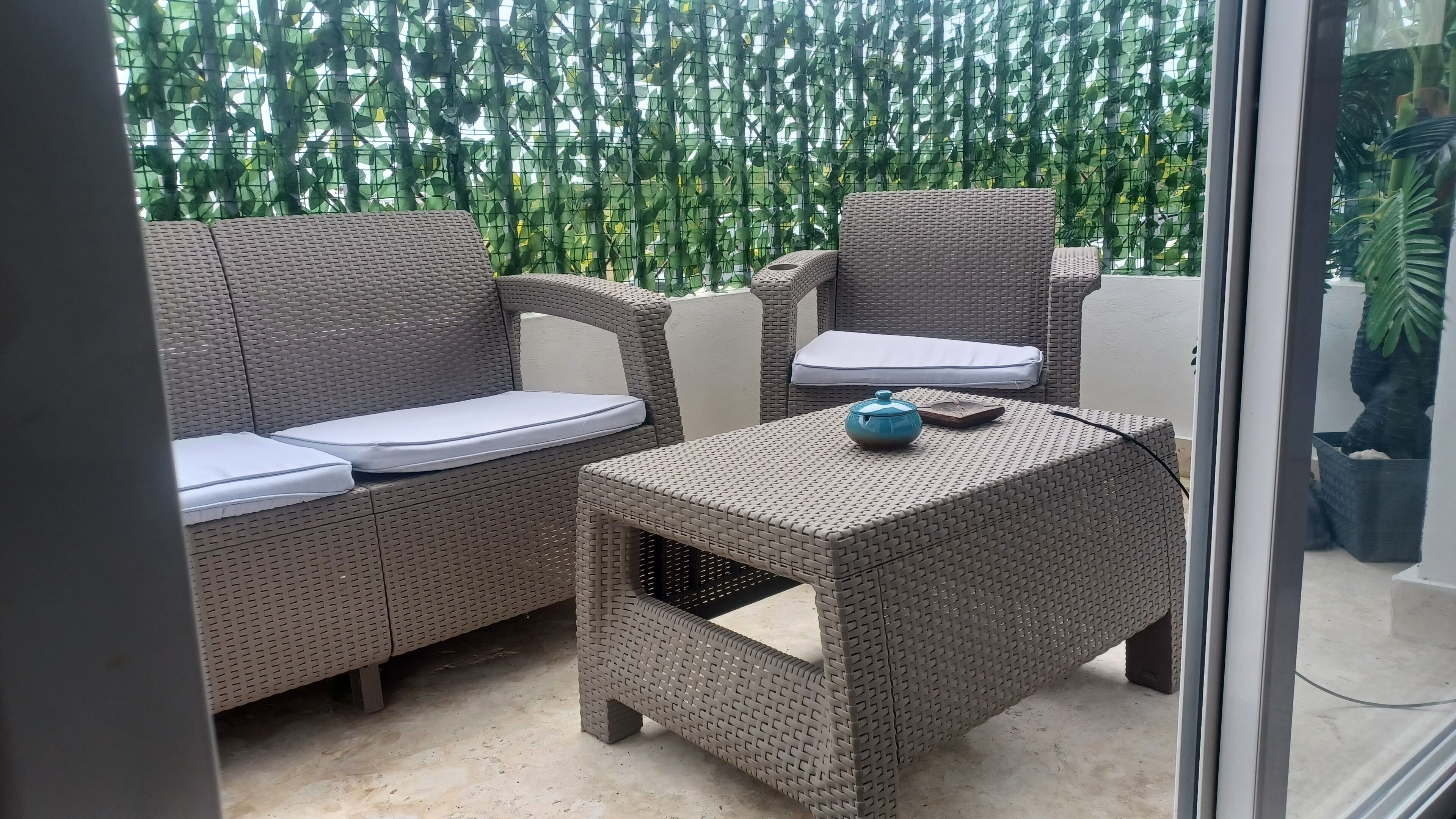 A balcony with wicker furniture, including a sofa and a chair, and a small table with a blue object on it.