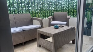 Een balkon met rieten meubilair, waaronder een bank en een stoel, en een klein tafeltje met een blauw voorwerp erop.