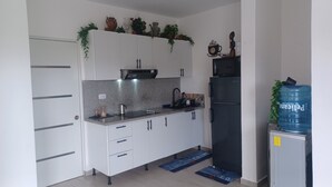 Een kleine keuken met witte kastjes, een zwarte koelkast, een waterdispenser en een koffieapparaat.