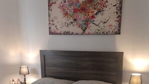 Een slaapkamer met een groot bed, twee nachtkastjes met lampen, een houten hoofdeinde, en een kleurrijk abstract schilderij aan de muur.