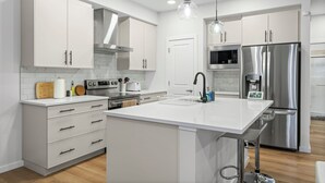 Una cuina moderna amb armaris blancs, electrodomèstics d'acer inoxidable i una illa central amb rentatge.