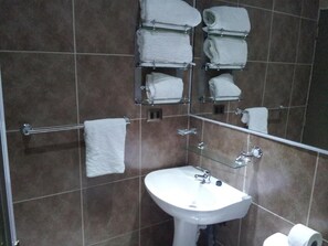 Ein Badezimmer mit einem weißen Waschbecken, einer Glasablage mit Handtüchern und einer Duschkabine aus Glas.