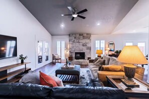 Uma sala de estar ampla com lareira, sofás de couro e ventoinha no teto.