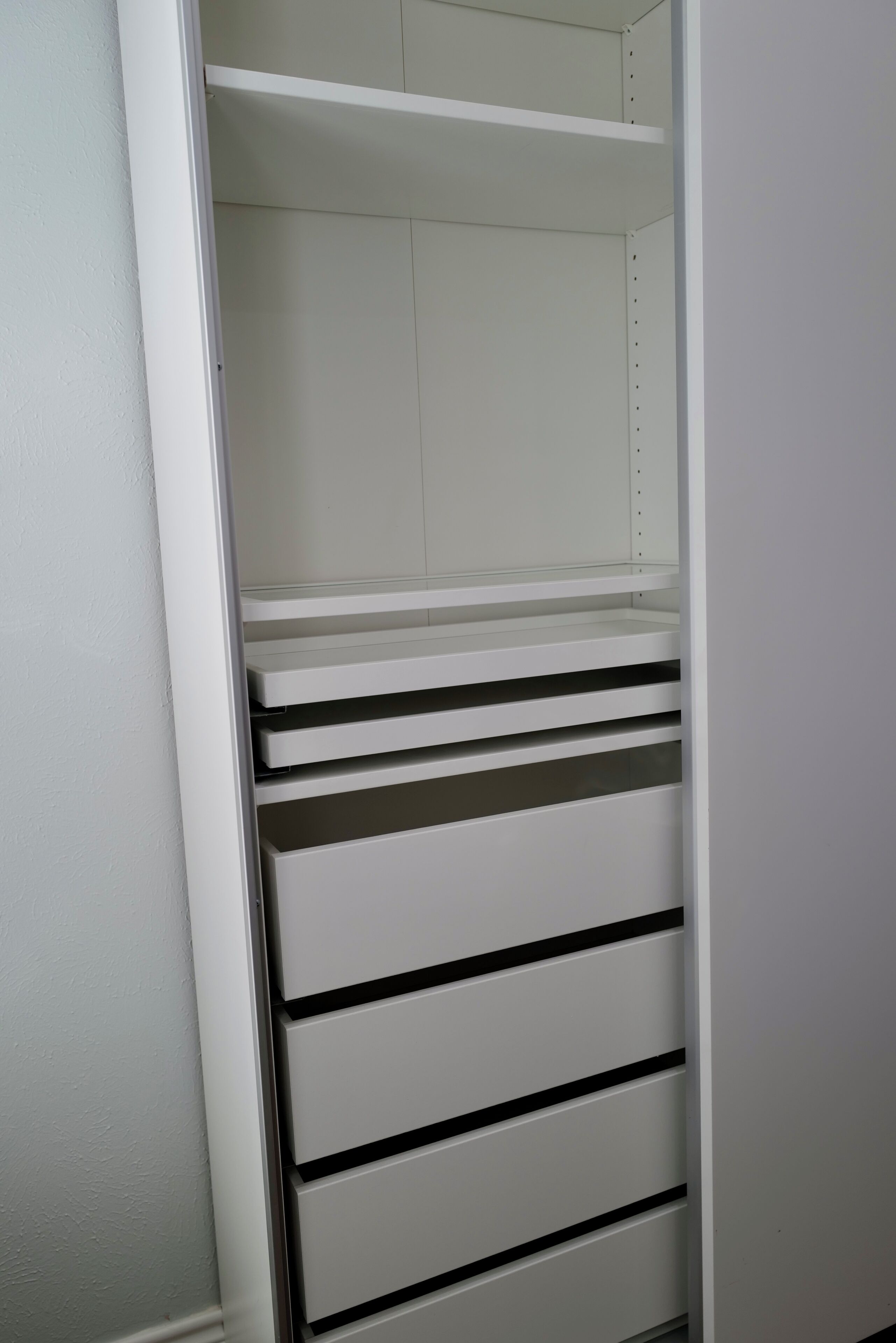 Ein weißer Kleiderschrank mit mehreren Regalen und Schubladen.