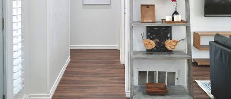 A hallway with a wooden floor, a gray bench, a shelf with decorative items, and a 'home' sign on the wall.
