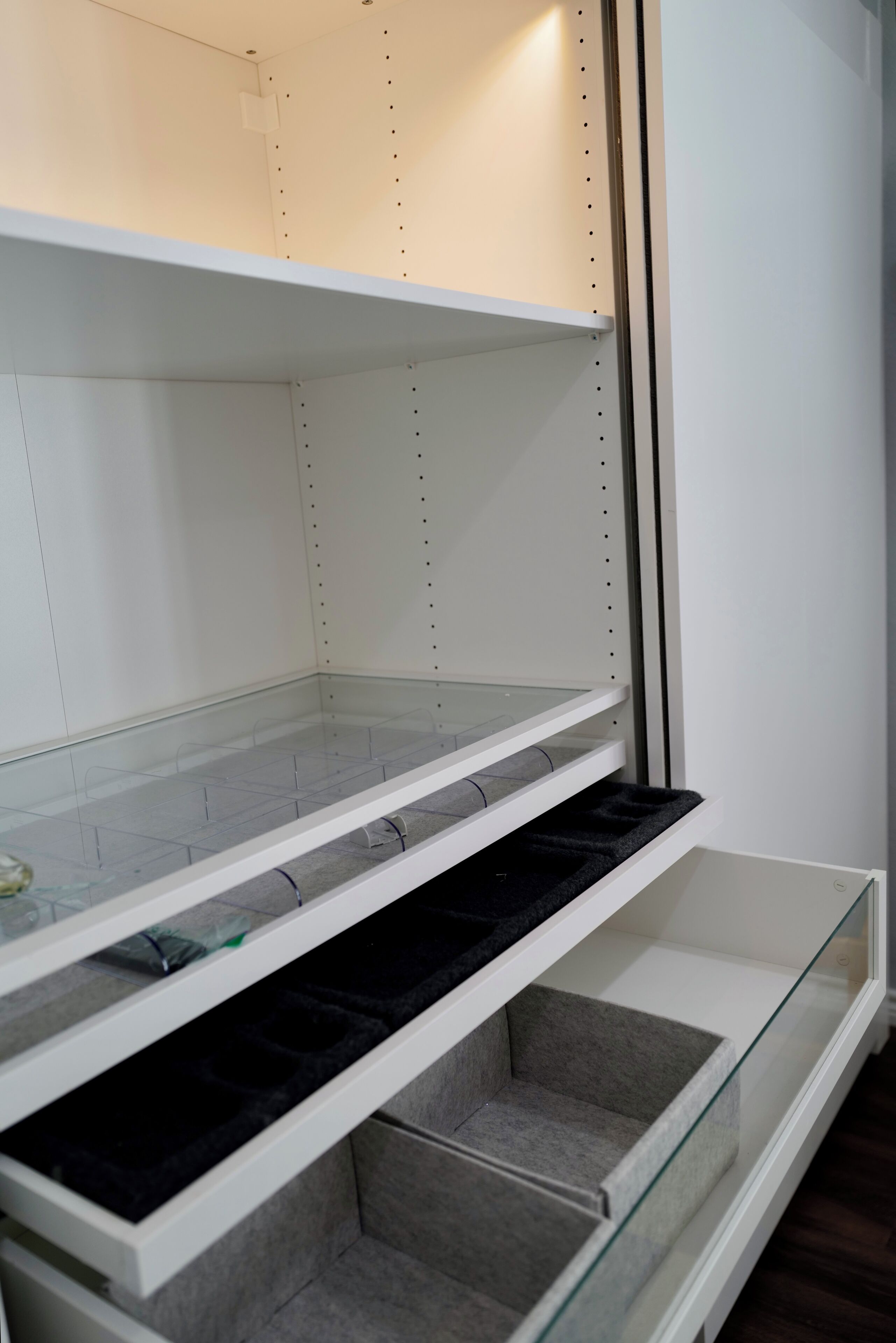 A room with white walls, a glass door, and a white shelf unit with multiple compartments.