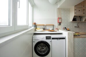 A compact kitchen with a built-in washer and dryer, a window, and a tiled backsplash. - Central Cascais 1BDR With Balcony Near The Beach (Cascais)